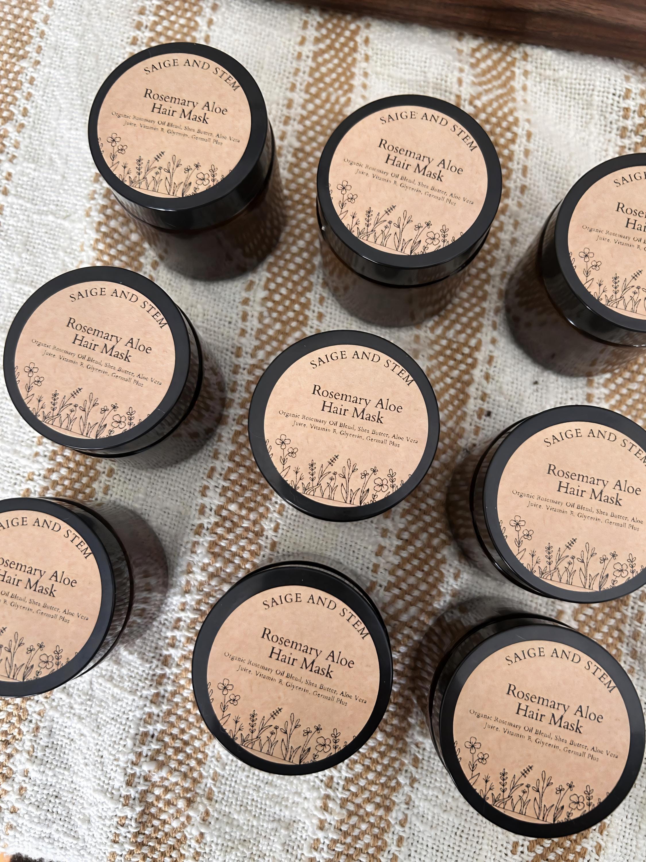 Rosemary Aloe Hair Mask in dark jars with botanical labels, arranged on a textured surface.