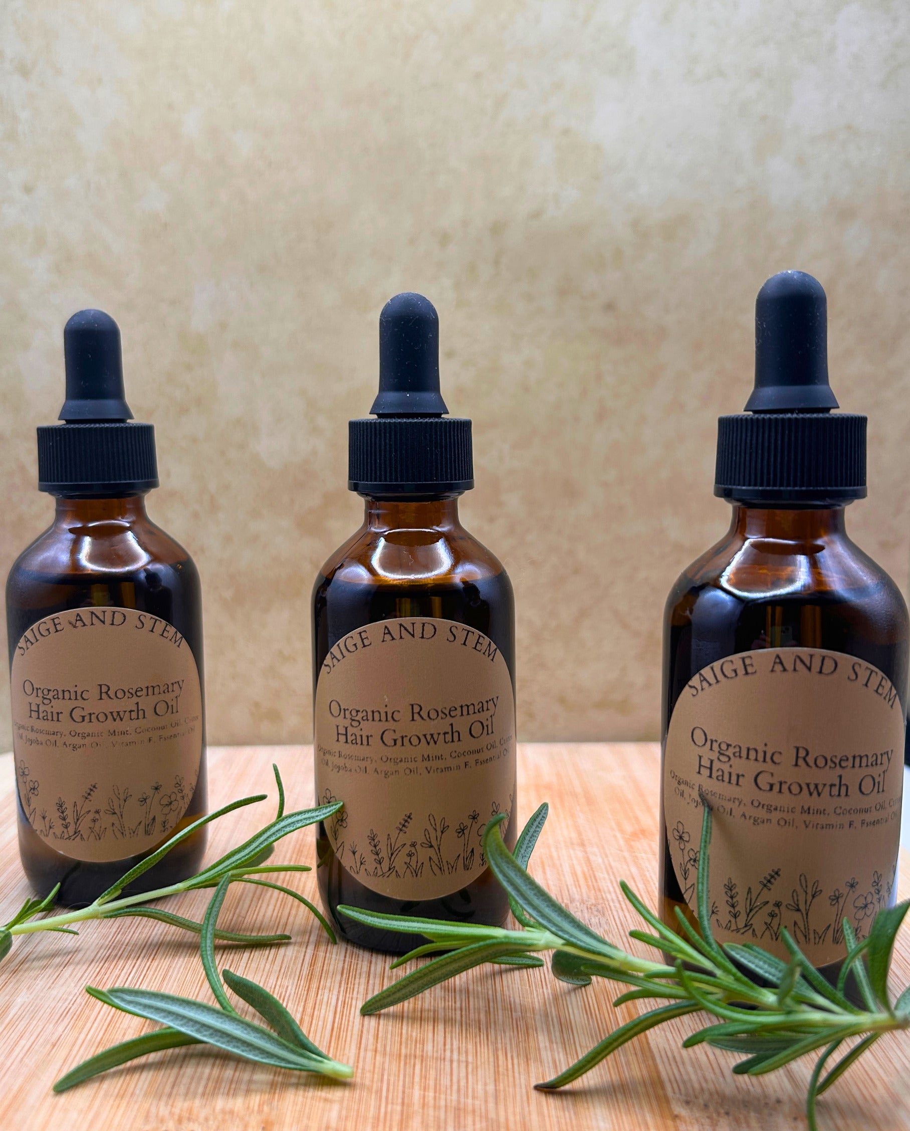 Rosemary Hair Growth Oil in amber bottles with droppers, surrounded by fresh rosemary sprigs.